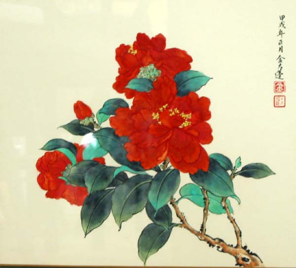 Red Camellia blossoms on a branch.